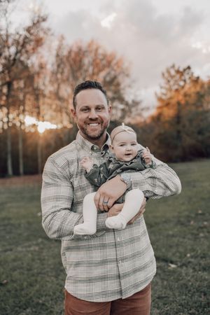 Outdoor autumn portrait of parent holding baby against backdrop of fall foliage.