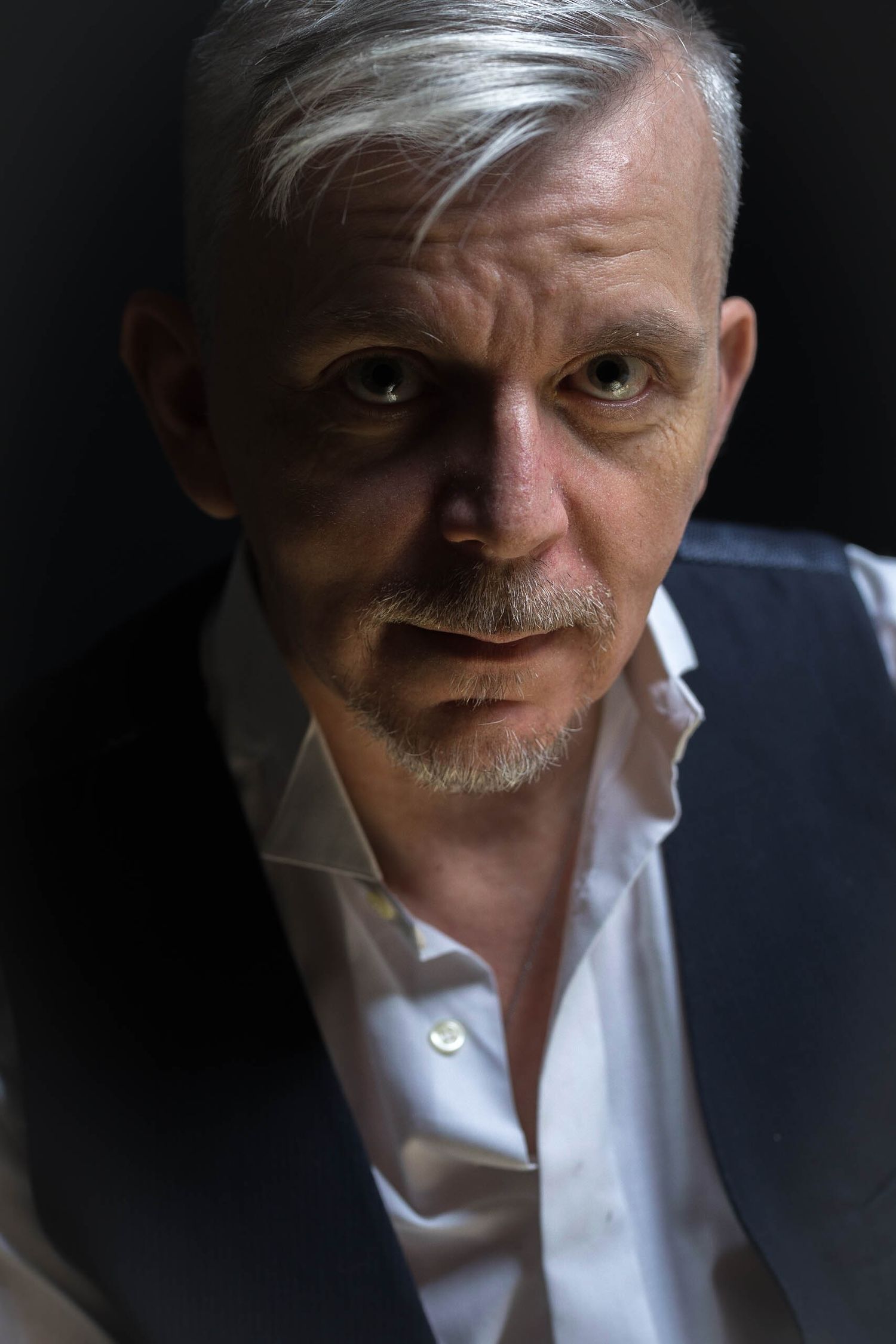A dramatic portrait shot in low key lighting showing a person wearing a white shirt against a dark background.