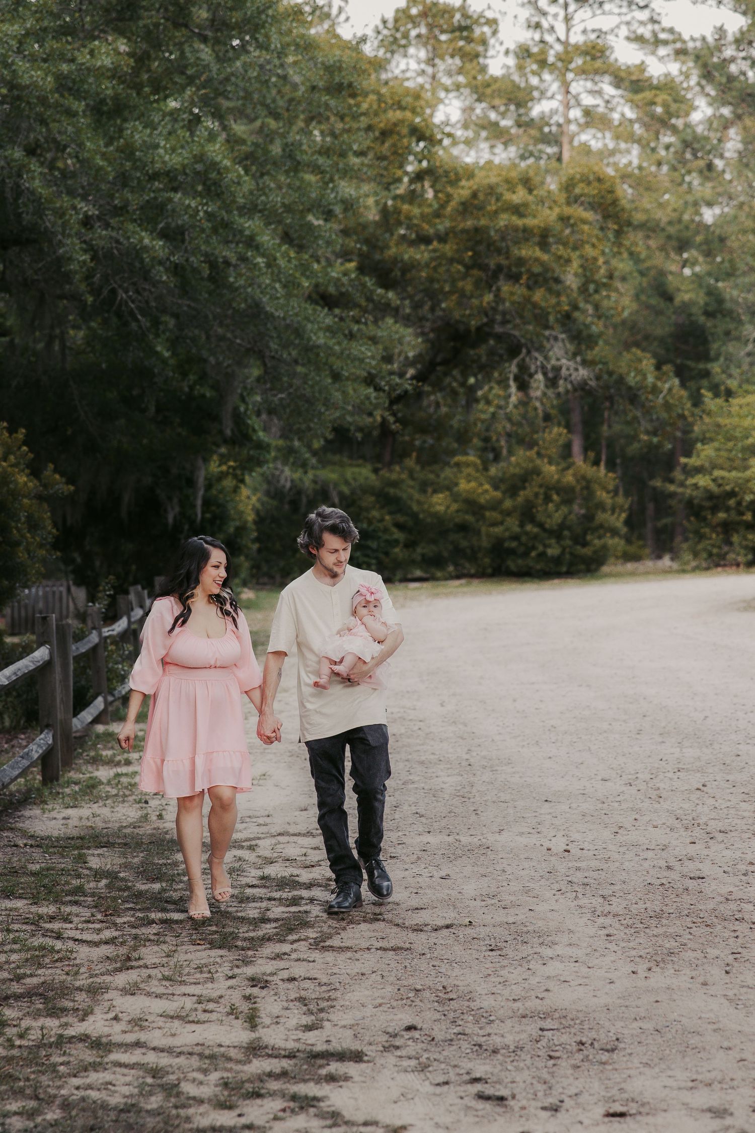 Couple walking hand in hand on dirt path with trees in background.