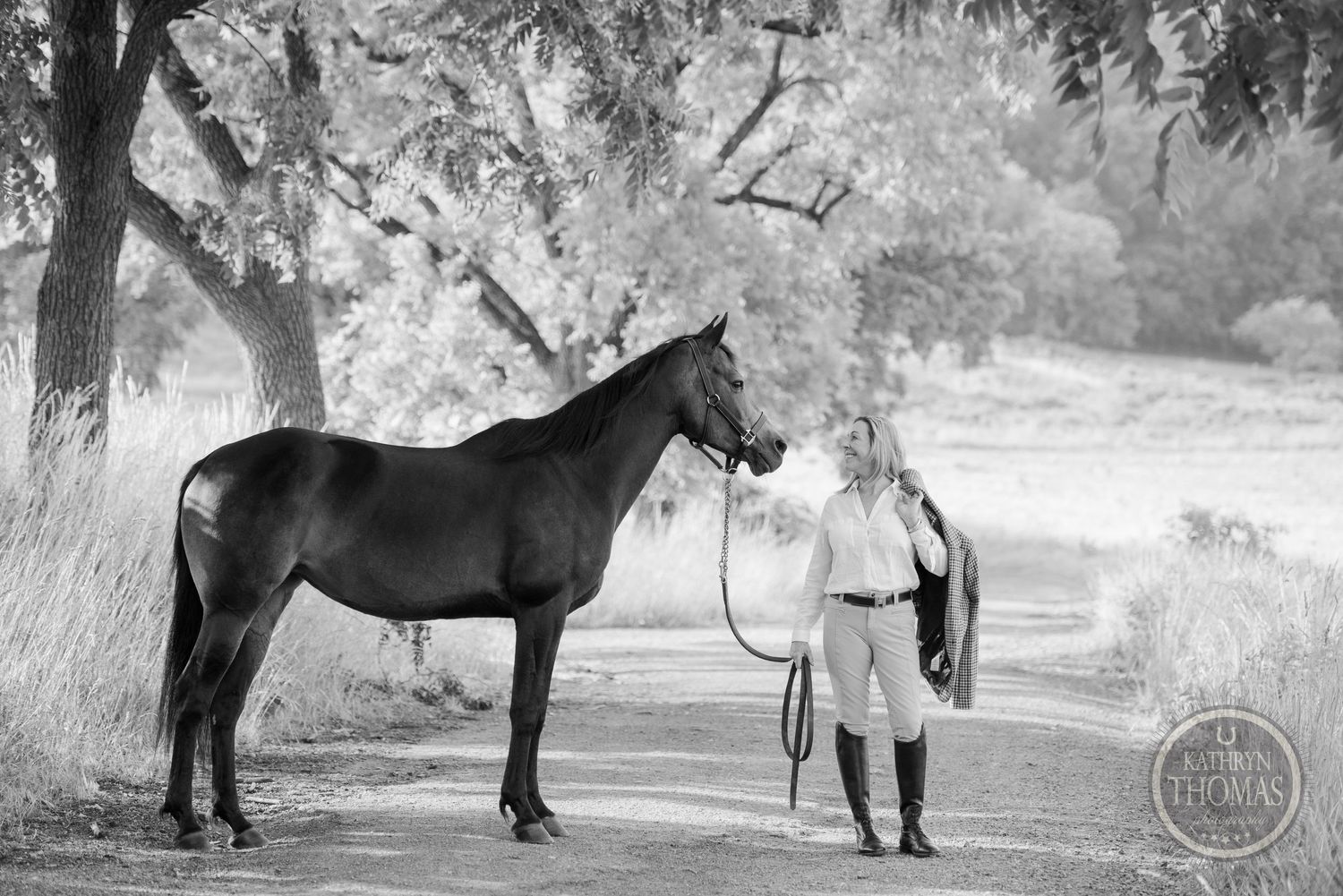 Black and white portrait of horse and handler on tree-lined path.