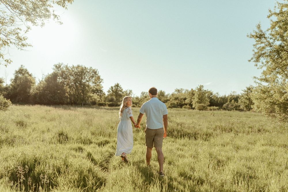 A couple walking hand in hand through a sun-drenched meadow at sunset.