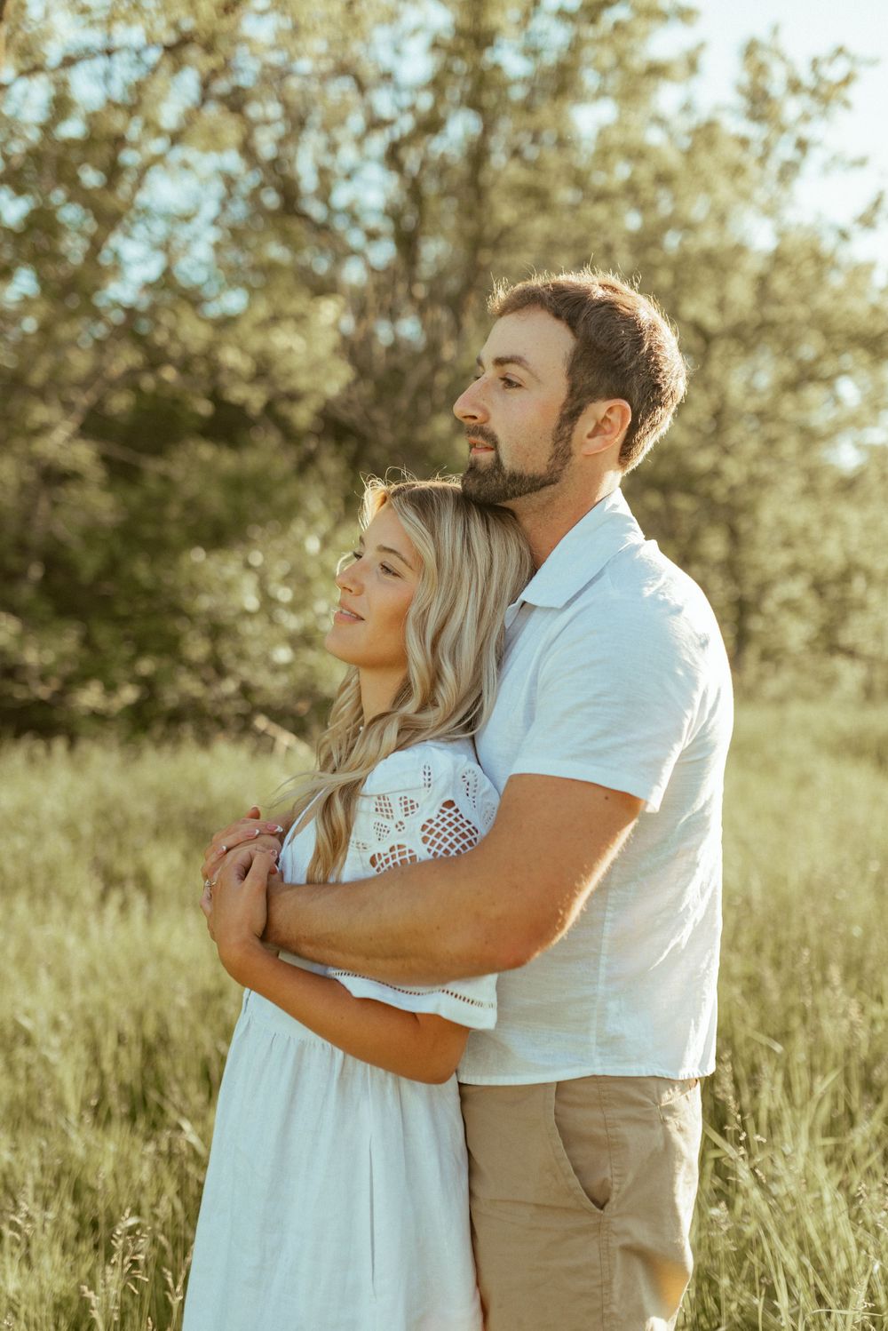 A tender embrace between a couple in a sunlit meadow with trees in the background.