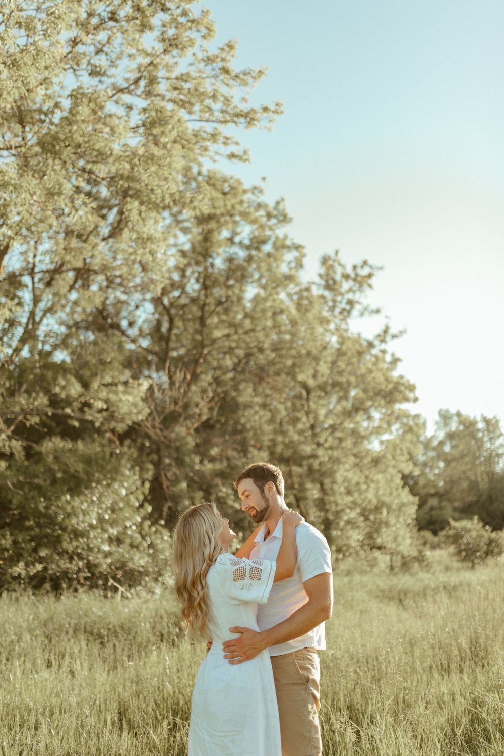 A loving couple sharing an intimate moment in a sunny field with blooming trees.