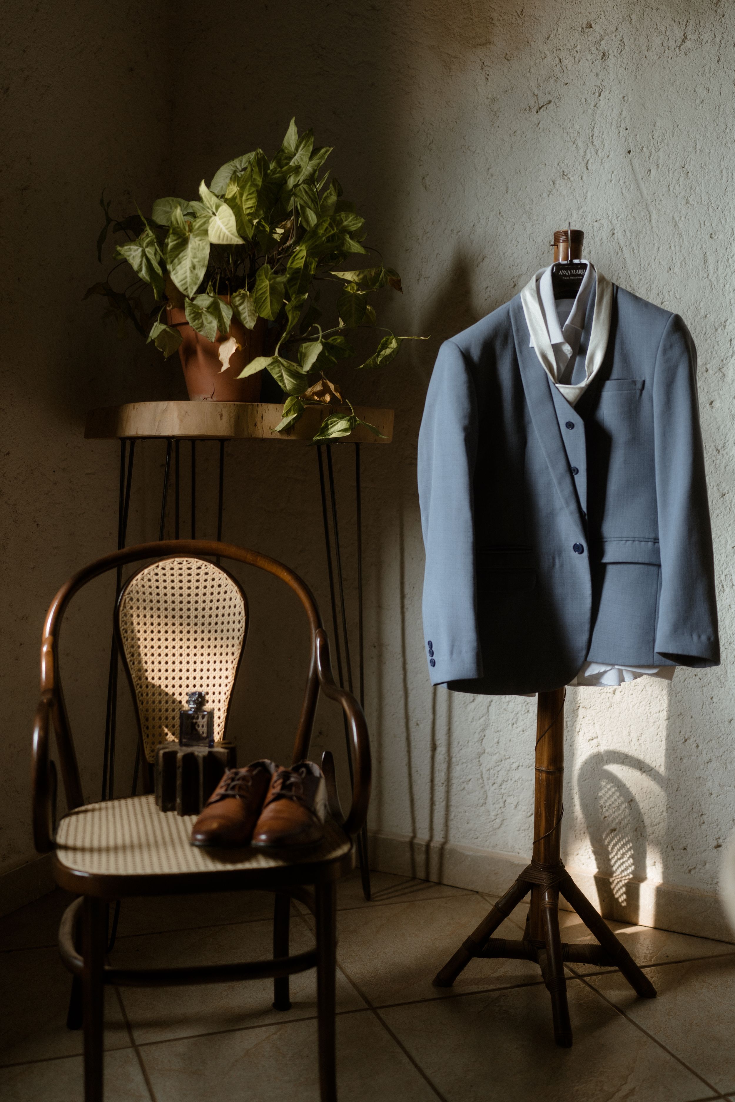 Gray suit jacket displayed on mannequin next to chair with brown shoes and floral arrangement.