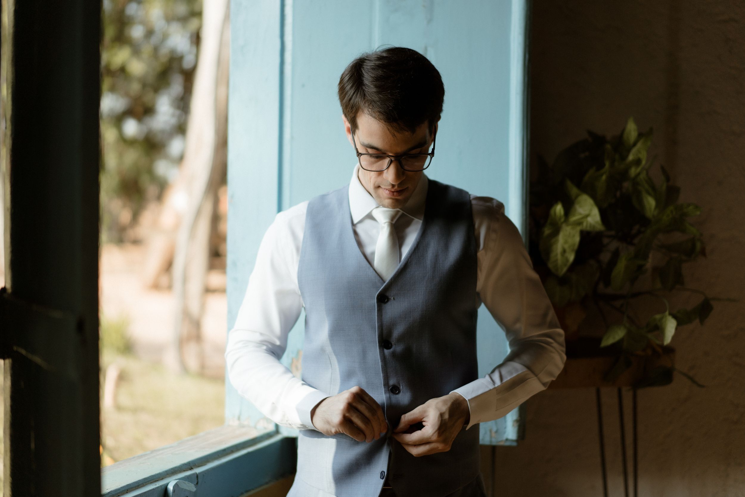 A formal vest being buttoned near a bright window.