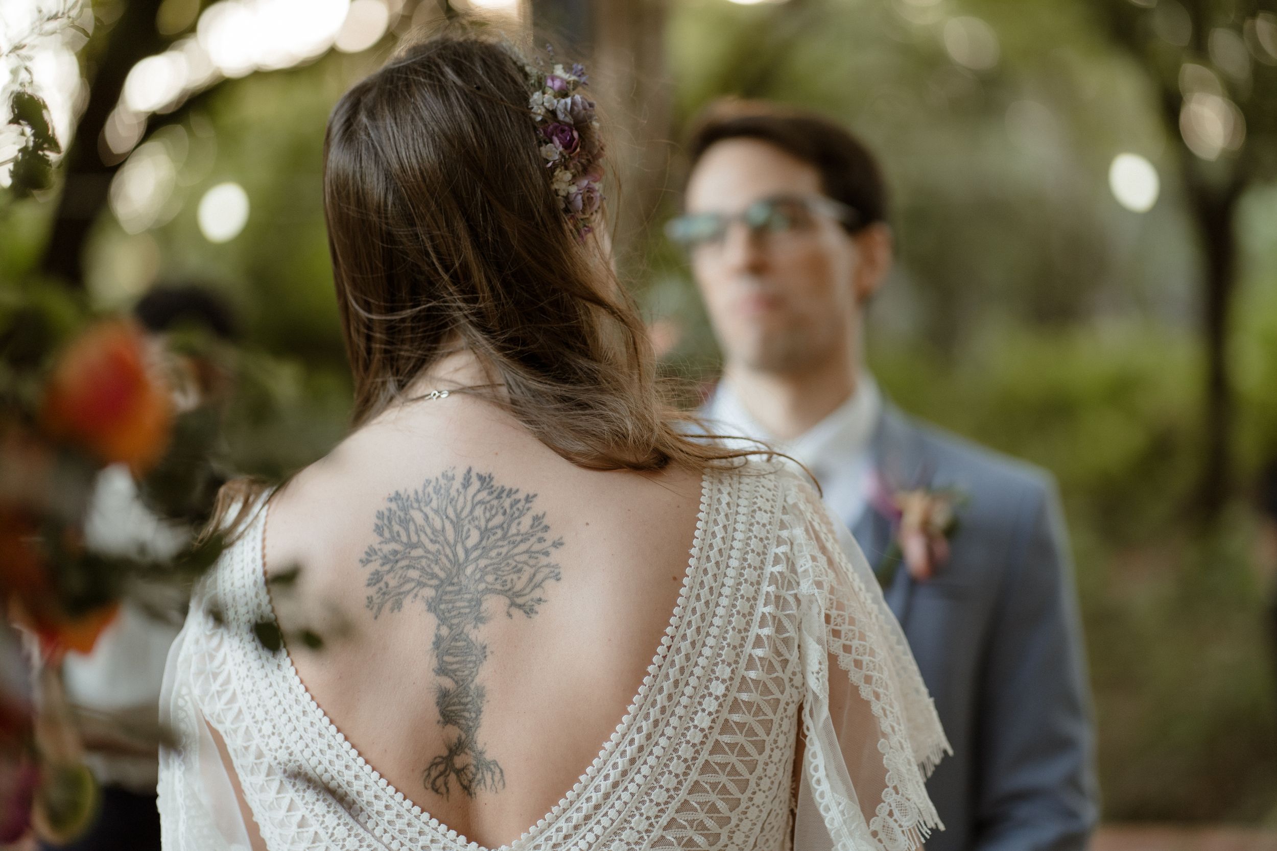 A detailed back view of a wedding dress reveals an intricate tattoo design and lace pattern.