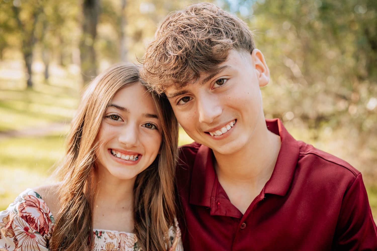 A young couple in burgundy and white outfits pose together outdoors during a fall photo session.