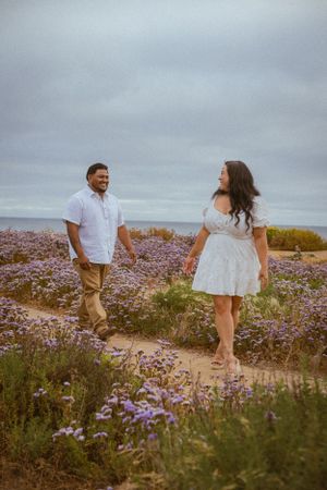 Couple walking and laughing together through a field of purple coastal wildflowers.