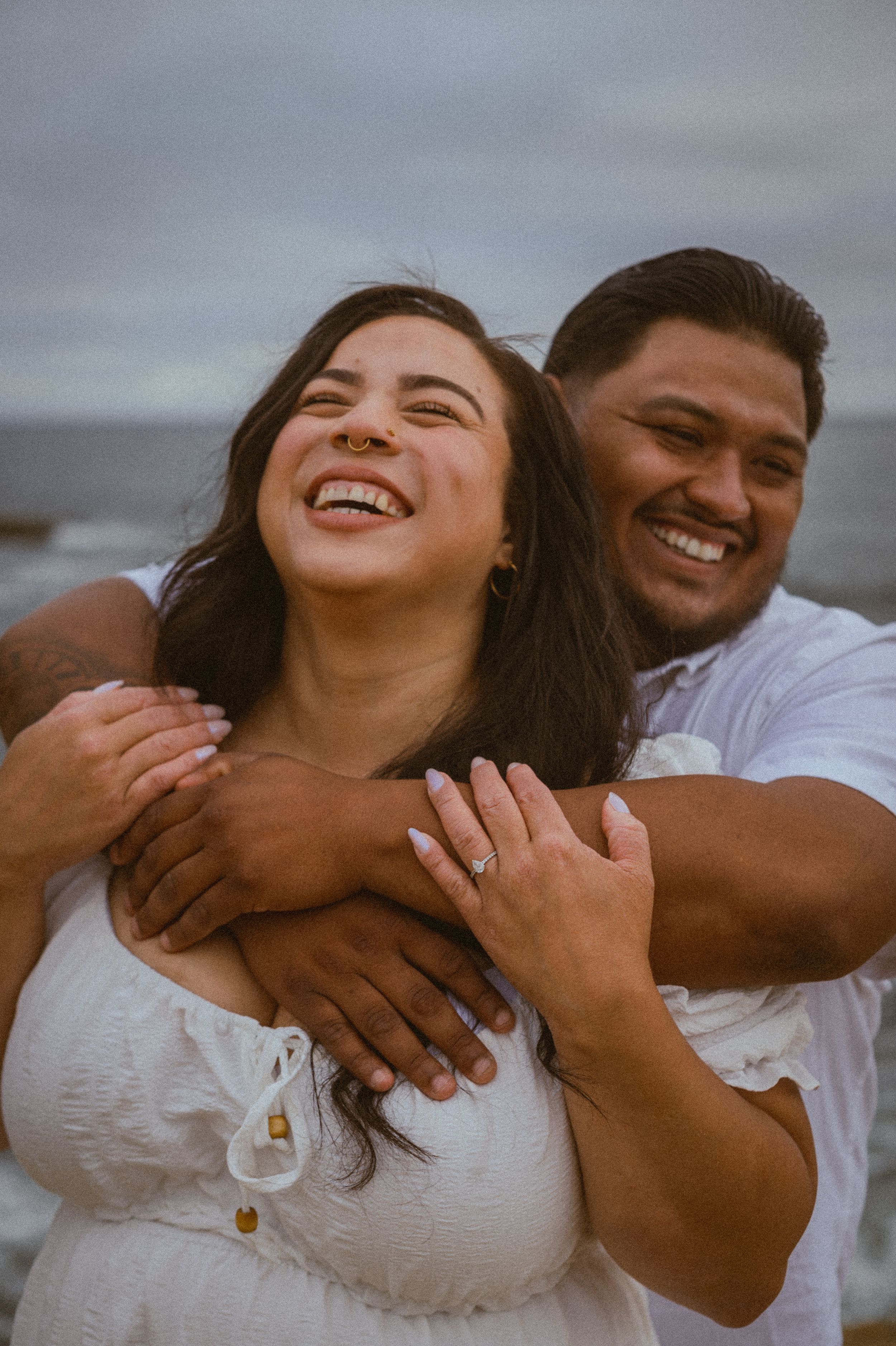 A joyful embrace filled with laughter on a cloudy beach day.