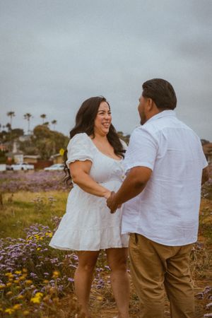 Playful couple in white outfits laughing together in a blooming wildflower field.