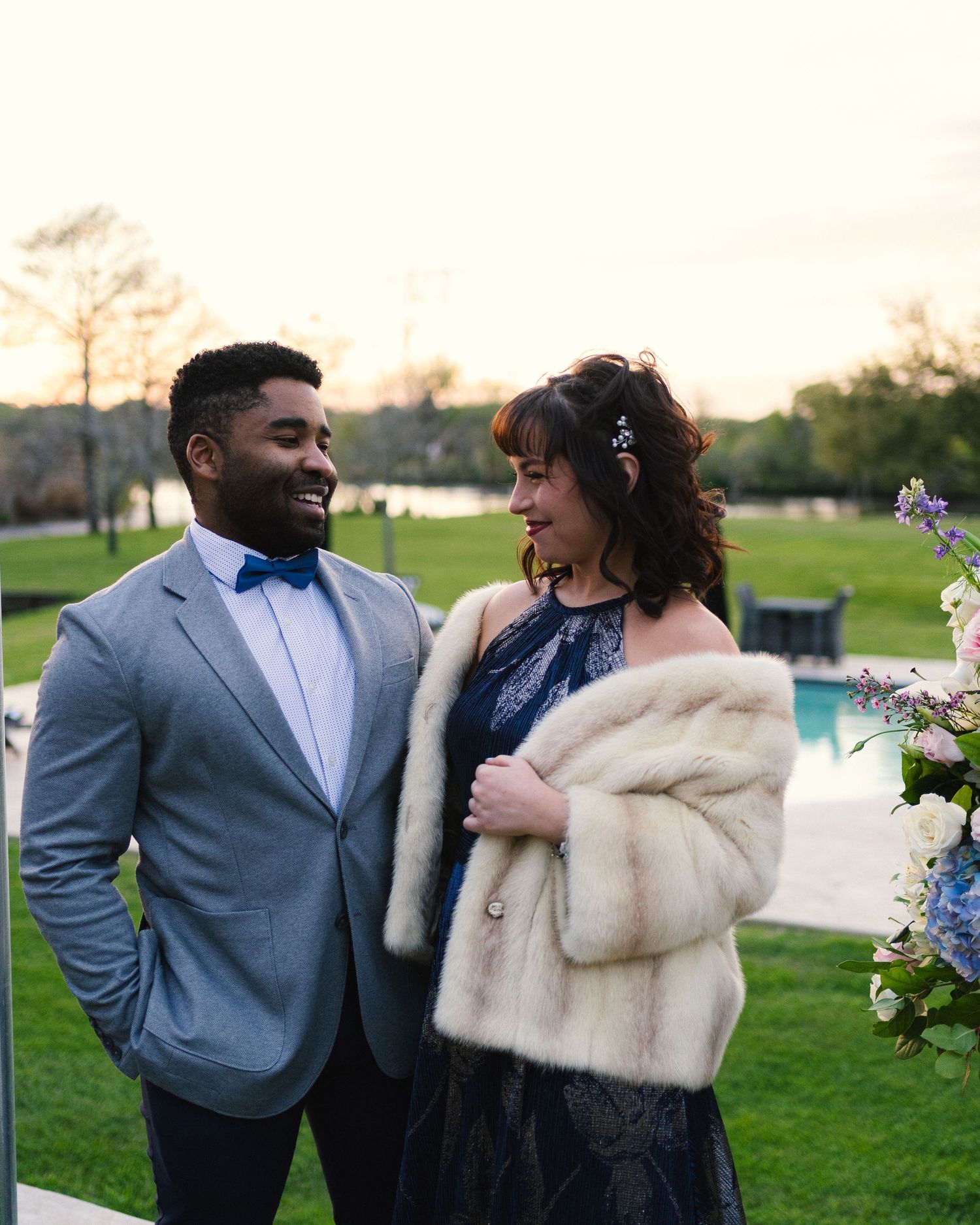 Elegantly dressed couple shares intimate moment at a wedding with floral decorations.