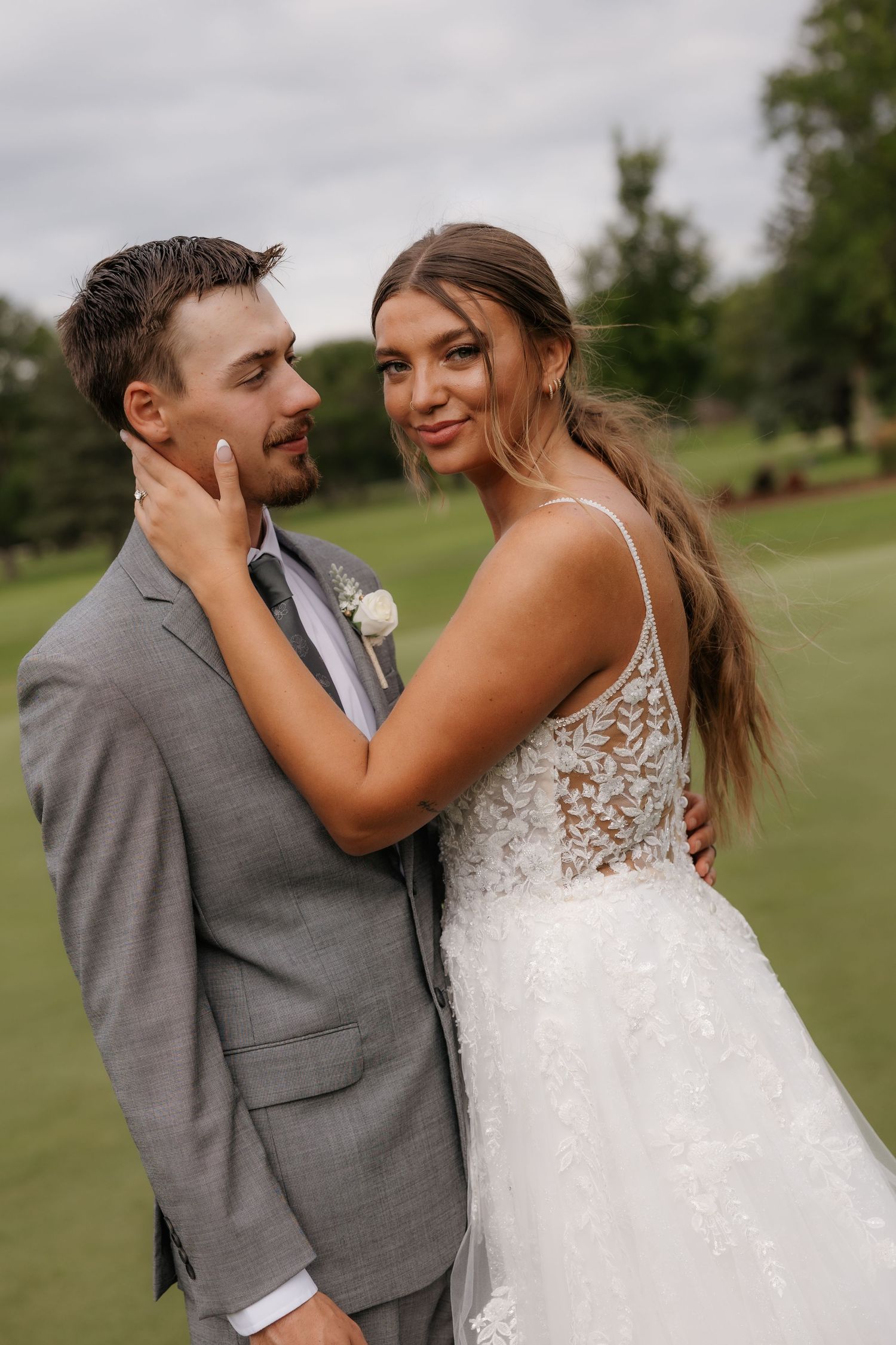 A newlywed couple shares a joyful moment on a hillside overlooking a scenic landscape.