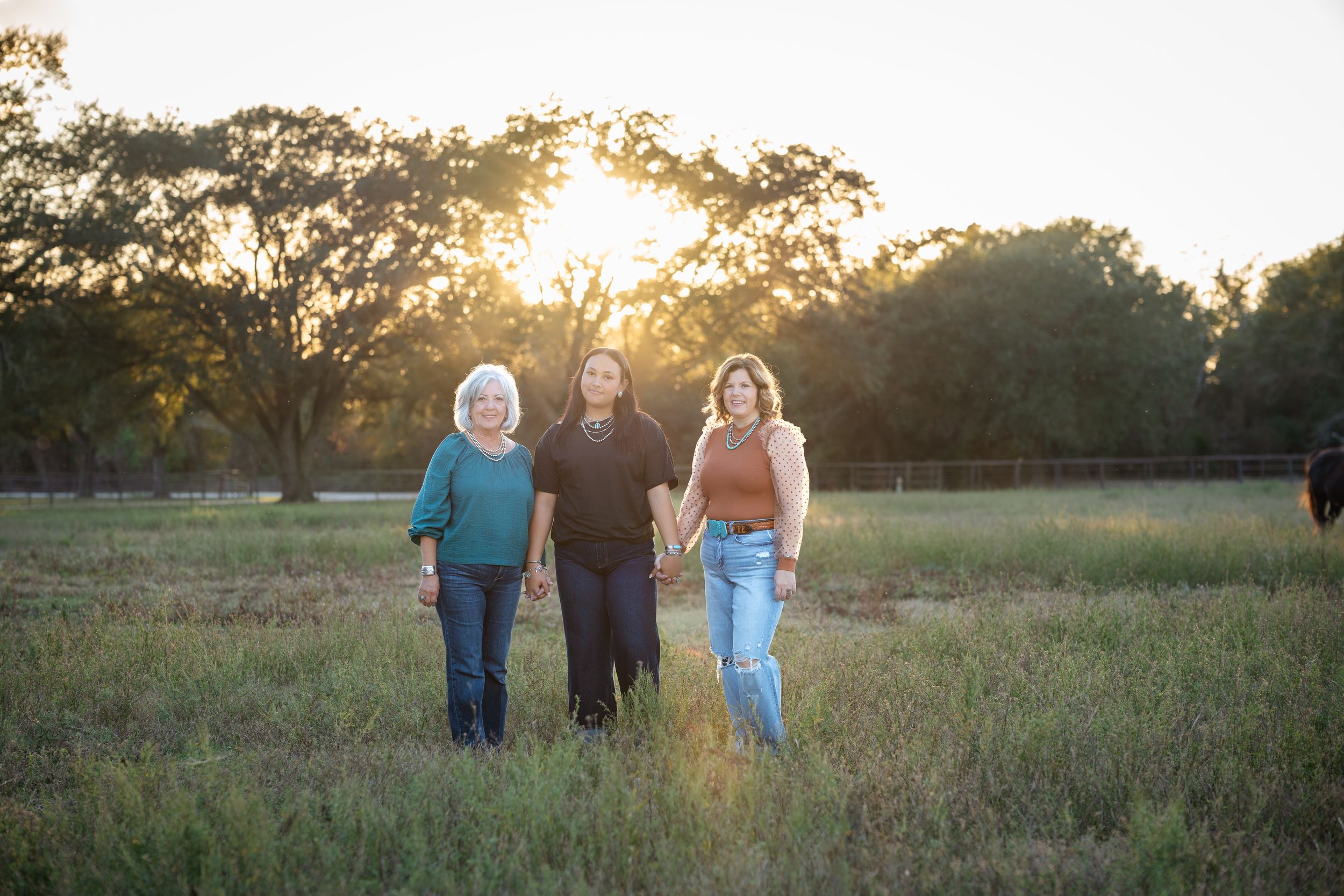 Family walks together through a grassy field at sunset with golden light filtering through trees in background.
