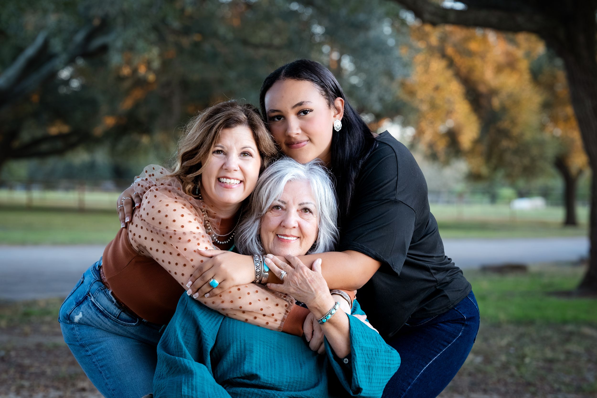 A group of people share warm embraces and laughter outdoors during a fall family photo session.