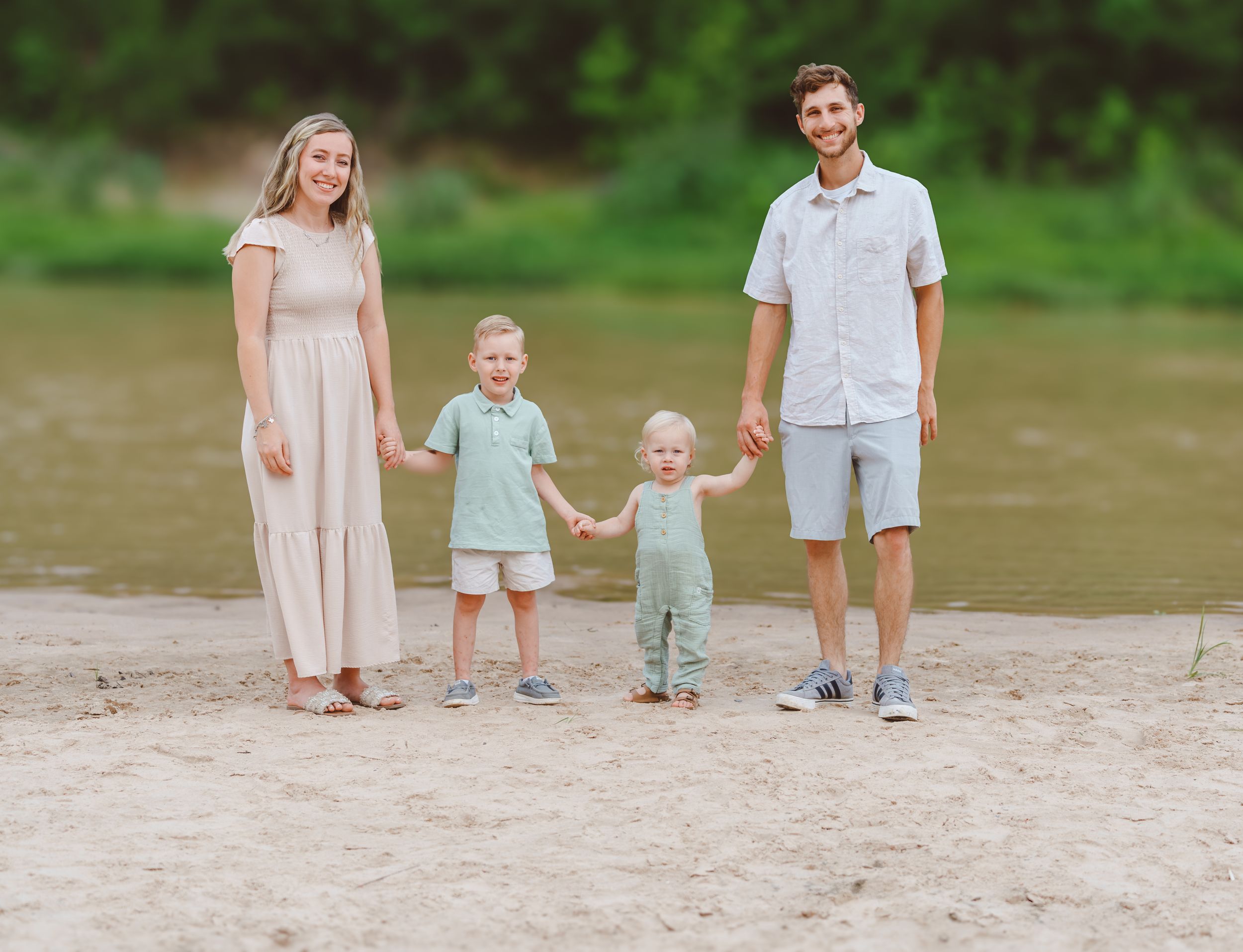 A family walks together along a sandy beach wearing soft pastel colors and coordinated casual outfits.