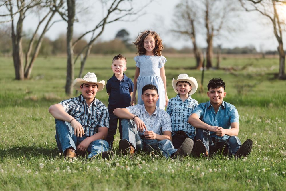 Group sits together in a grassy spring meadow wearing casual country attire with trees in background.