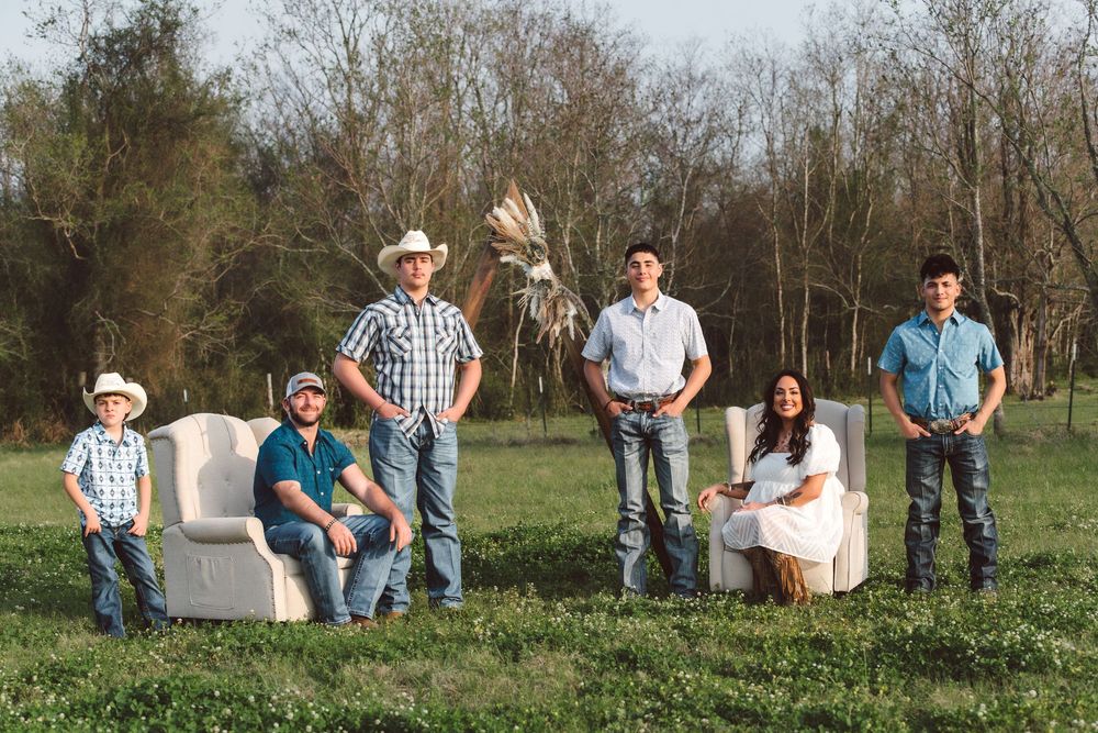 A group relaxes outdoors on a white sofa in a grassy field with trees in the background.