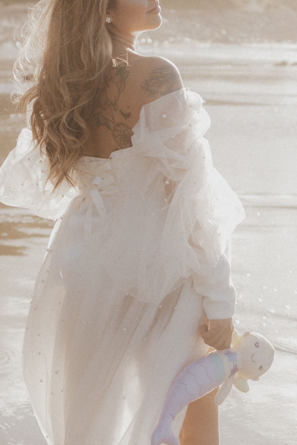Ethereal maternity portrait in flowing white dress on sandy beach.
