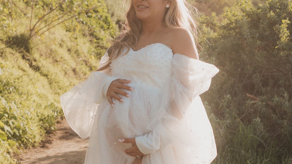 Sun-drenched maternity photograph on hiking trail wearing romantic white dress.