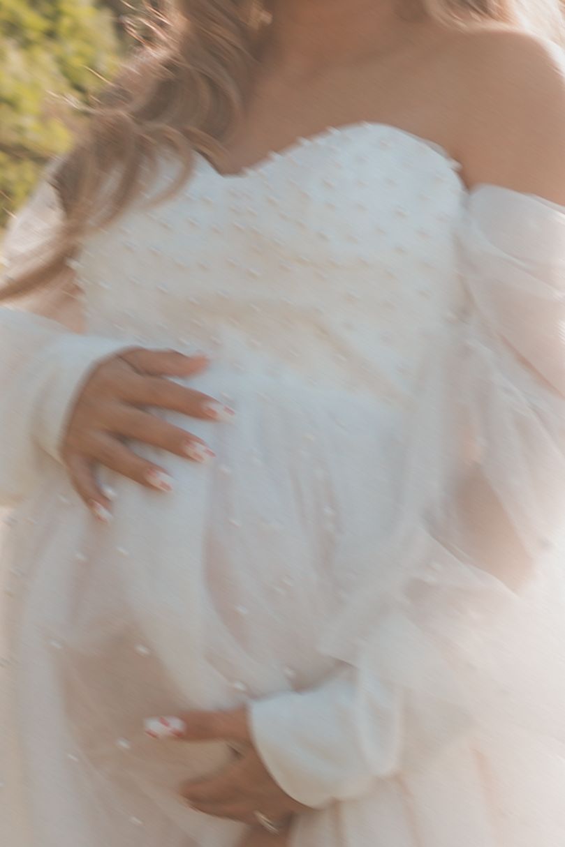 Close-up detail of textured white maternity gown with off-shoulder design.