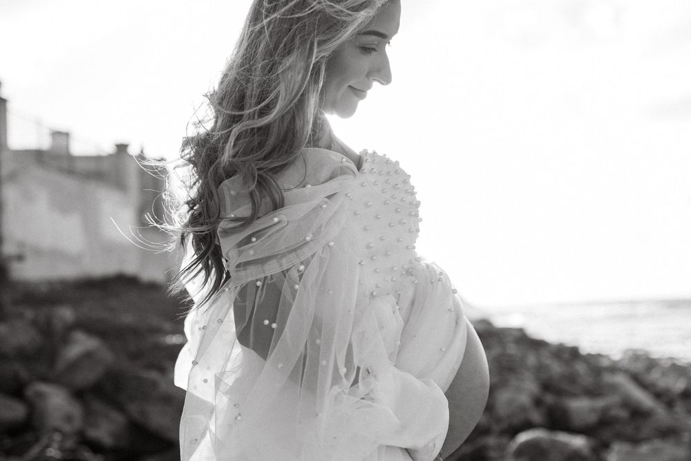 Artistic black and white seaside maternity portrait with rocky coastline.