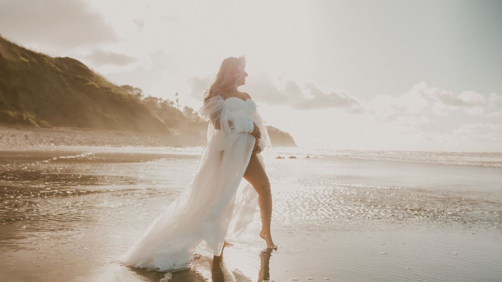 A flowing white dress catches the wind during a sunset beach photoshoot.
