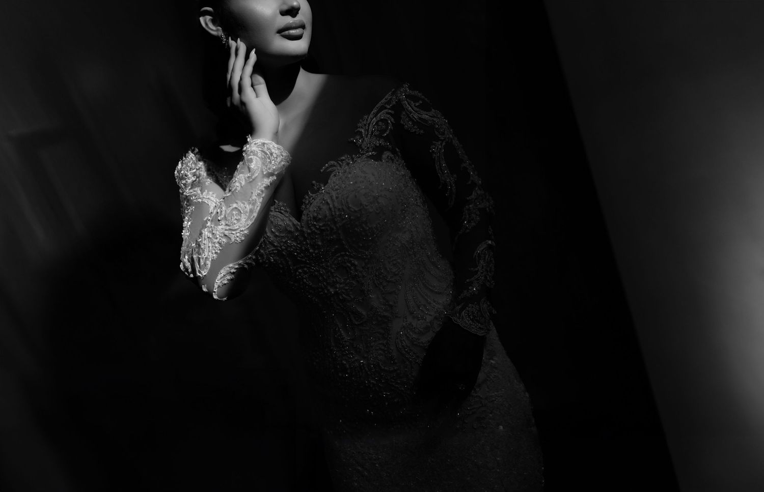Elegant bride in lace long-sleeve wedding gown poses in dramatic black and white portrait.