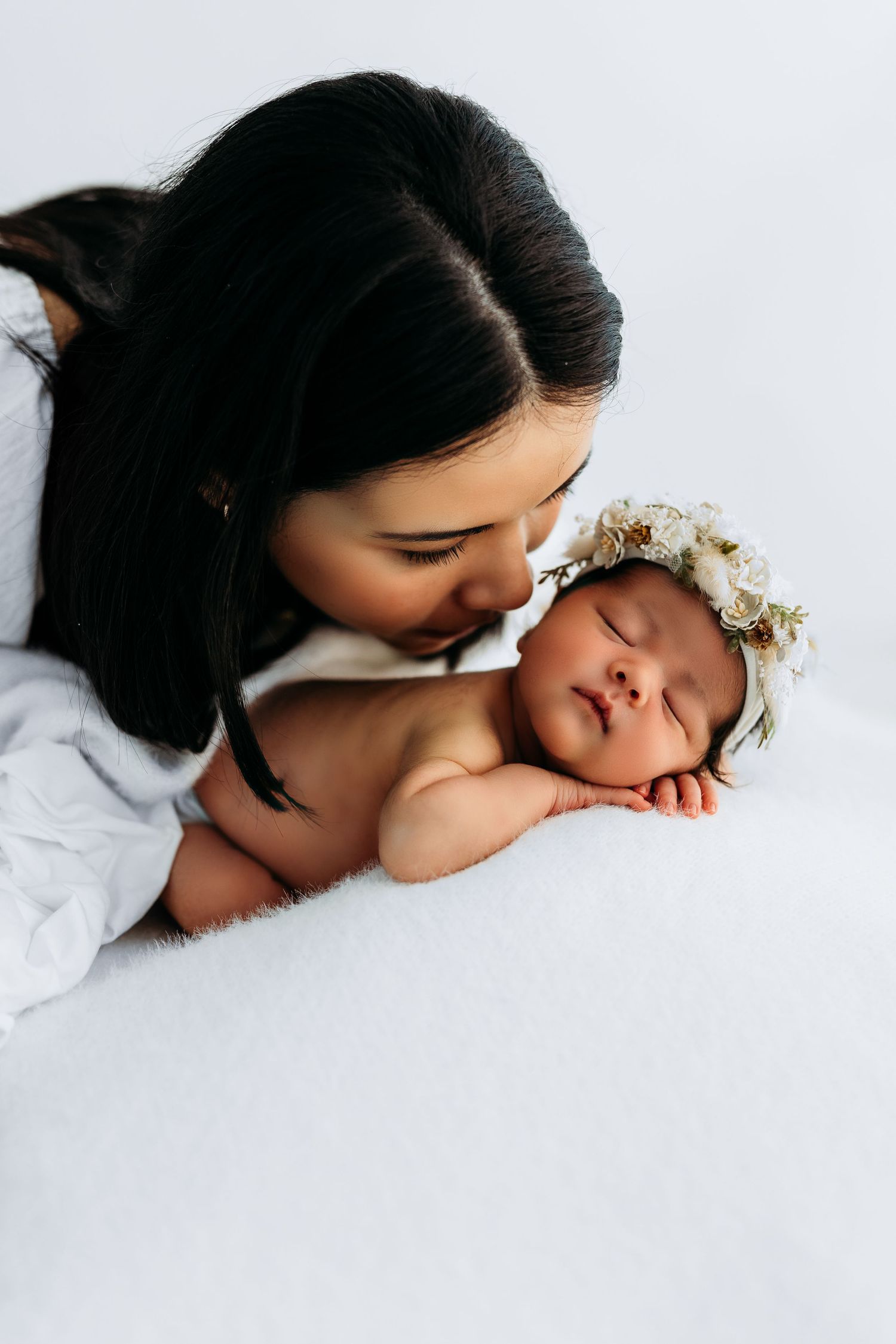 A tender moment shows a sleeping newborn wearing a floral headband being gently kissed by someone bending over.
Rashinphotography-Nova DC