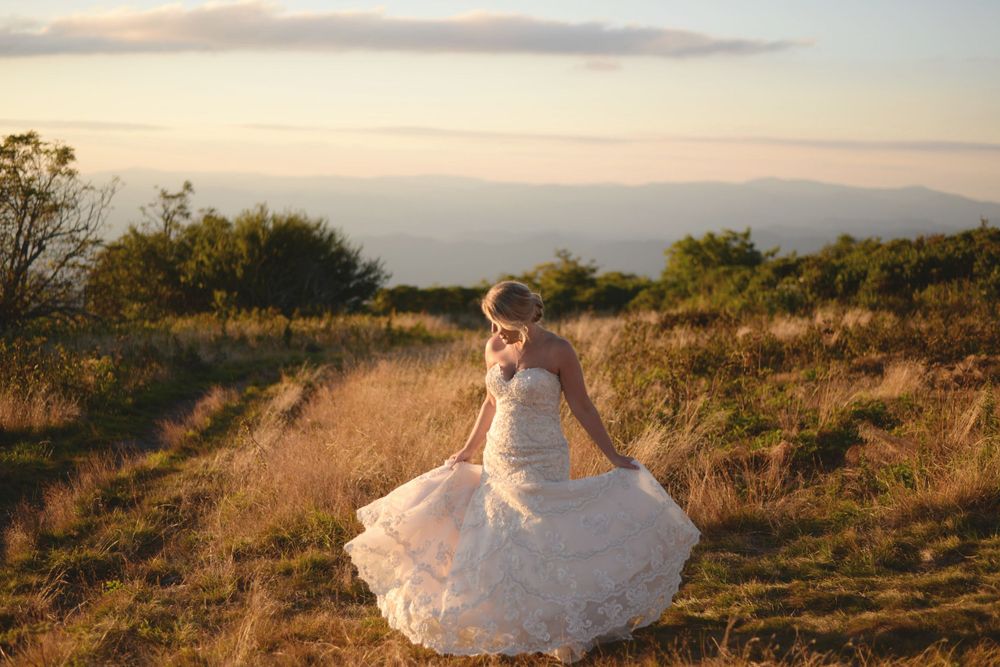 A bride spins her dress in golden light on a hilltop during sunset.