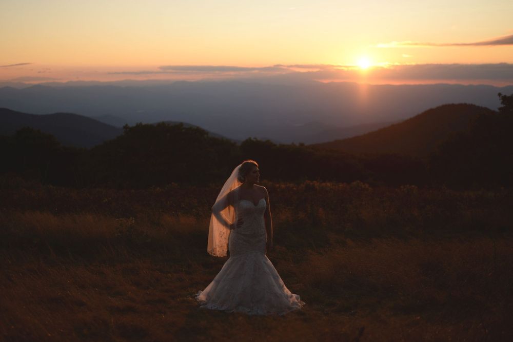 A bride in a white dress twirls against a stunning mountain sunset backdrop.