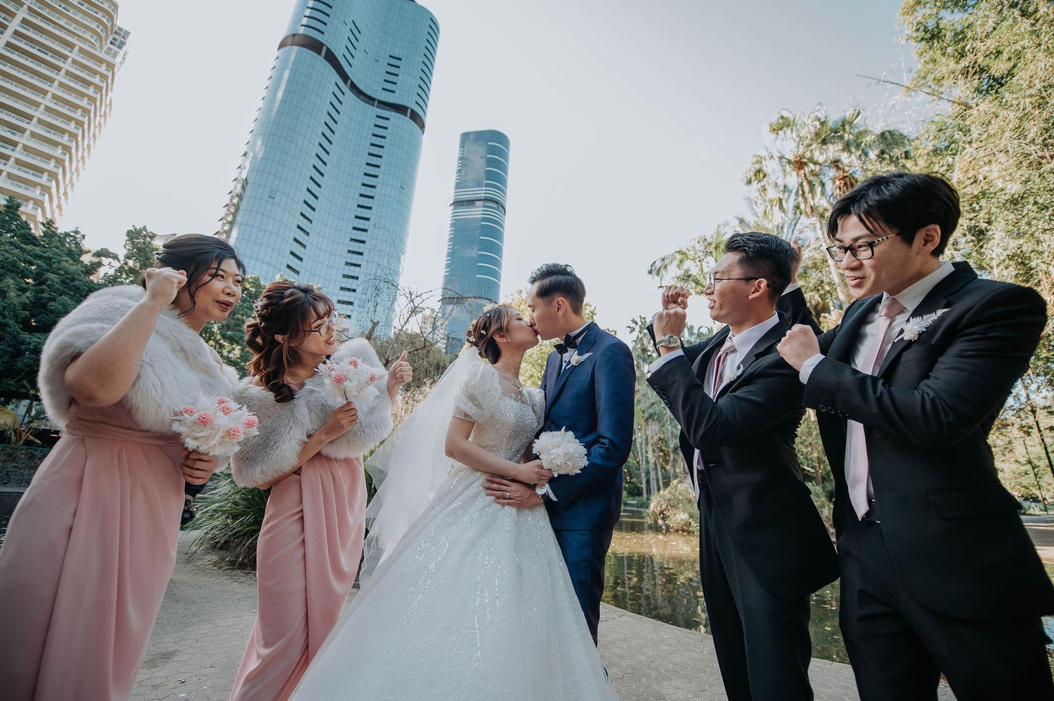 Wedding party poses playfully in urban setting with modern skyscrapers in background.