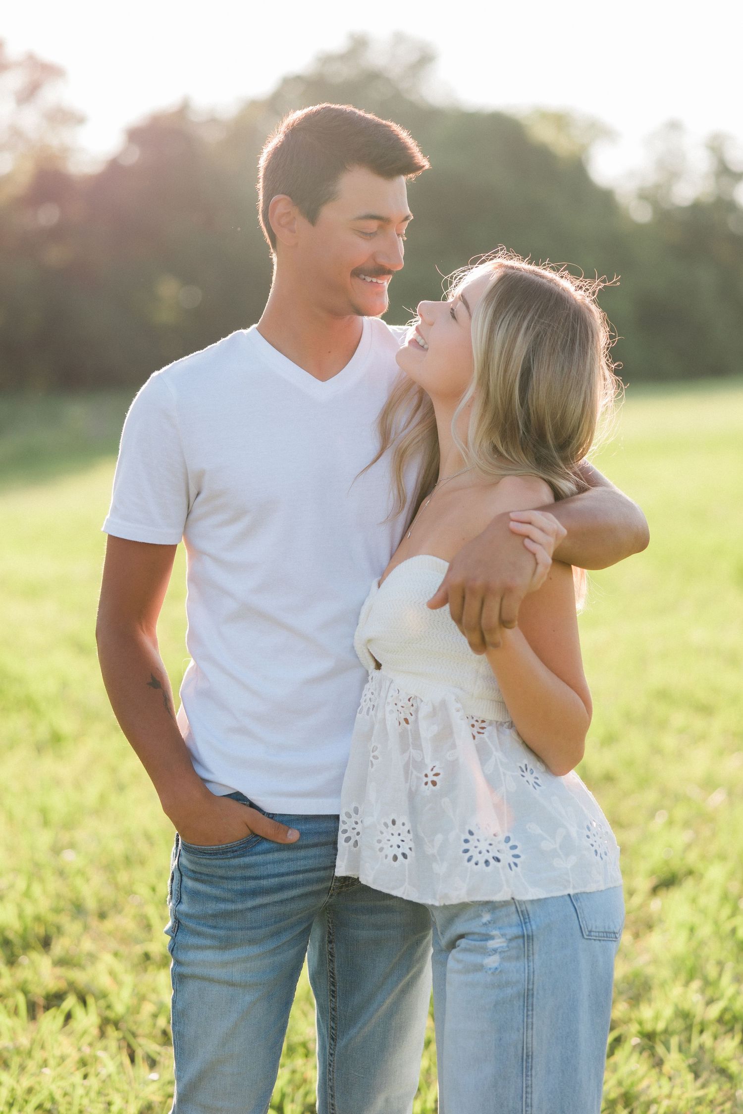A couple shares a joyful moment together in a sunny field.