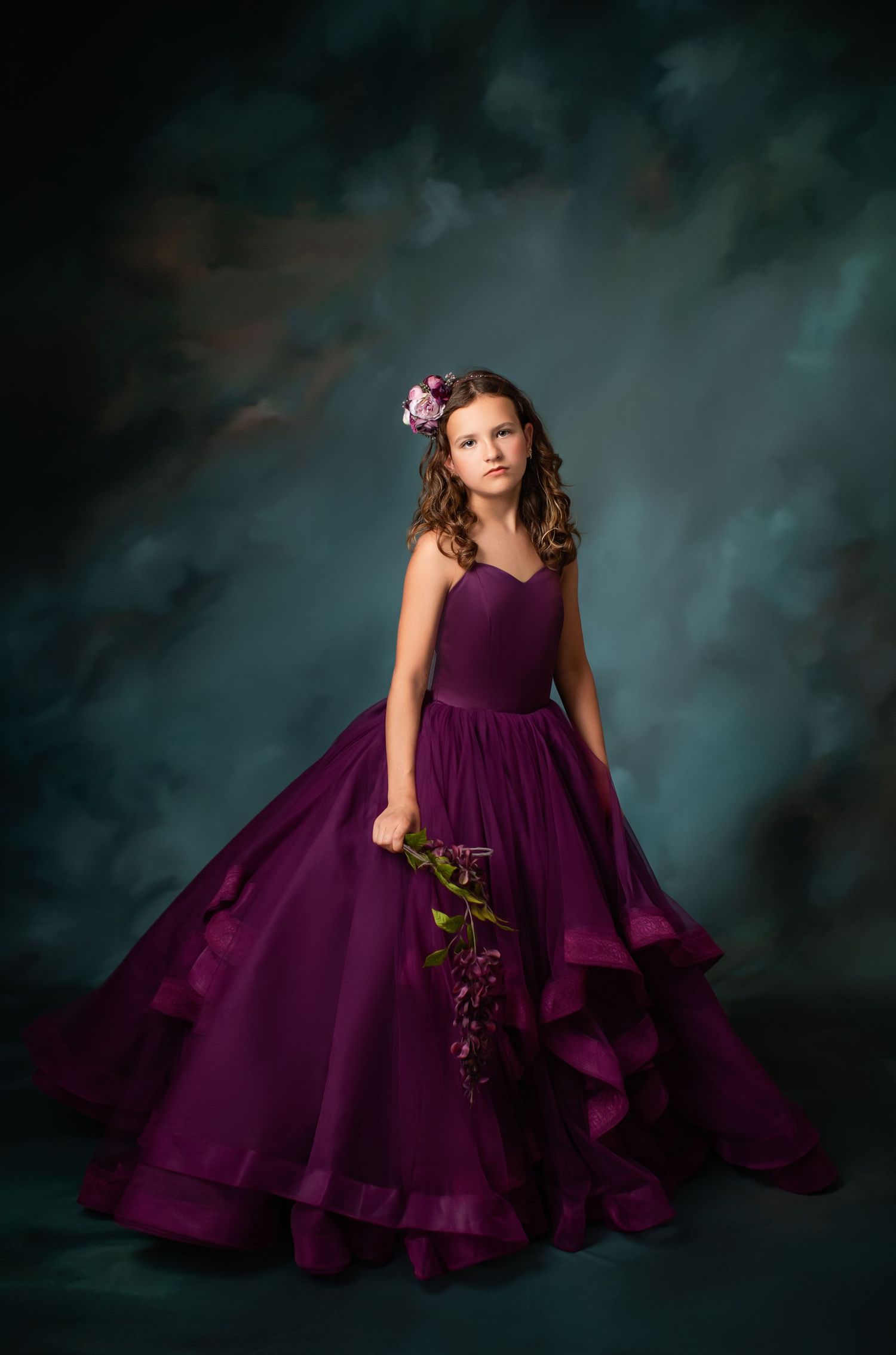Elegant portrait in flowing deep purple ballgown against dramatic dark background.