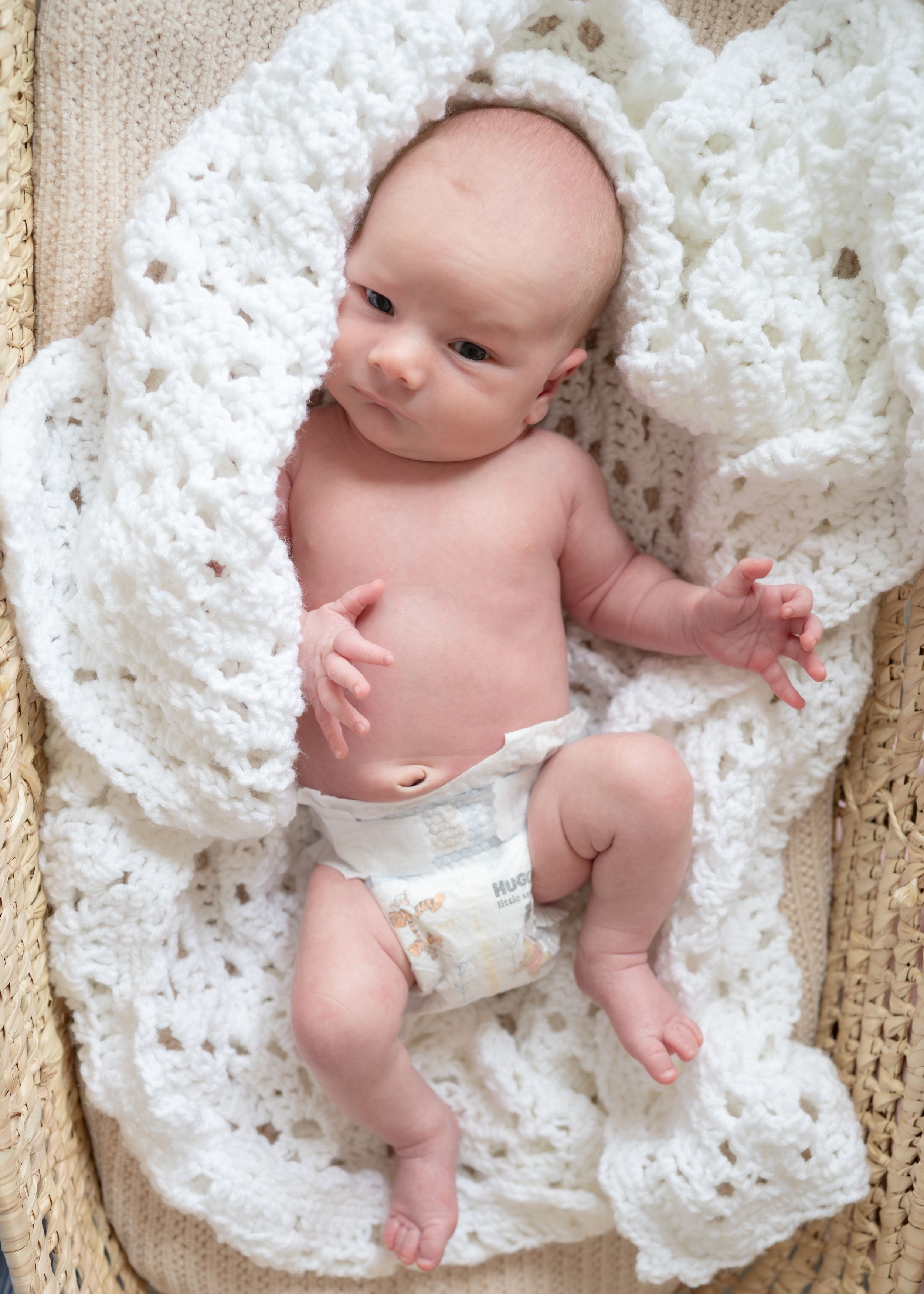 A close up shoot of a newborn laying on a white crocheted baby blanket in a Moses basket. Wrightstown NJ Maternity Newborn Photographer