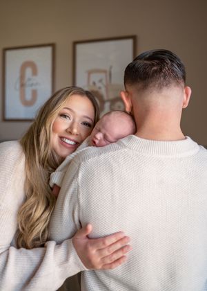 In home newborn session of dad holding baby on his shoulder and wife hugging from the side to be cheek to cheek with newborn.