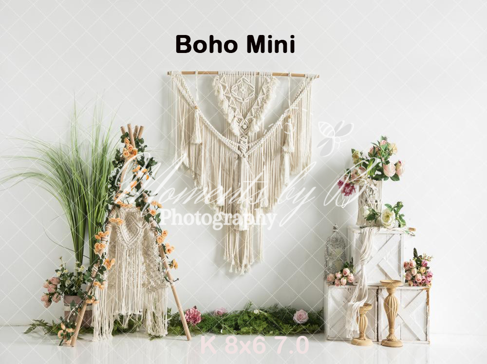 Boho-style wedding backdrop with macrame wall hanging, dried flowers, greenery and rustic wooden elements against white wall.