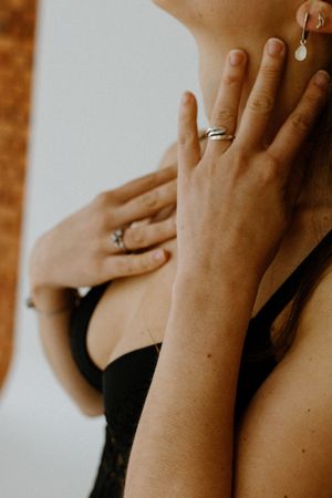 Close-up of two hands with silver rings resting on a woman's chest and neck, wearing a black lace top.