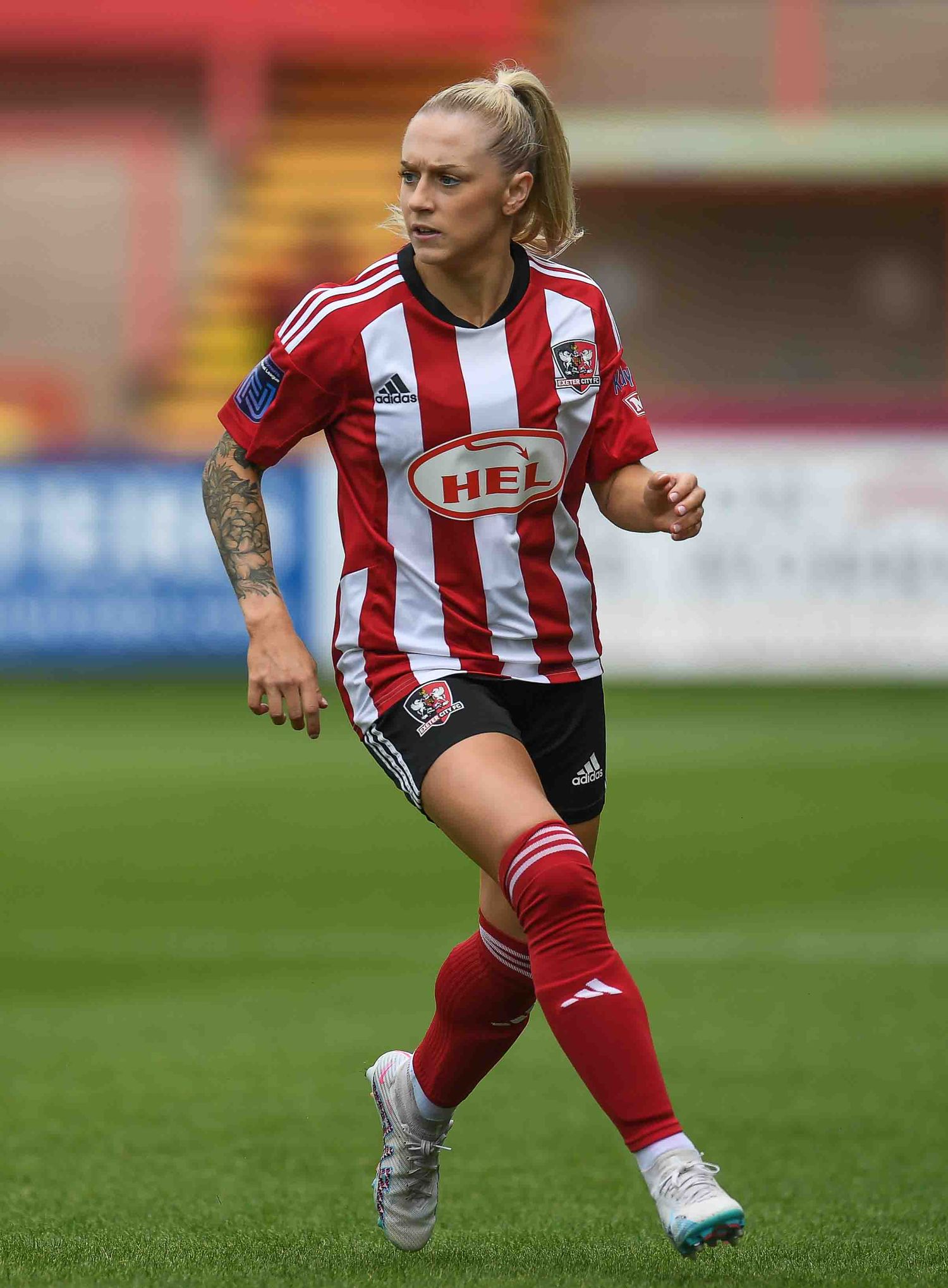 Soccer player in red and white striped jersey with tattoos runs on the field during a professional match.