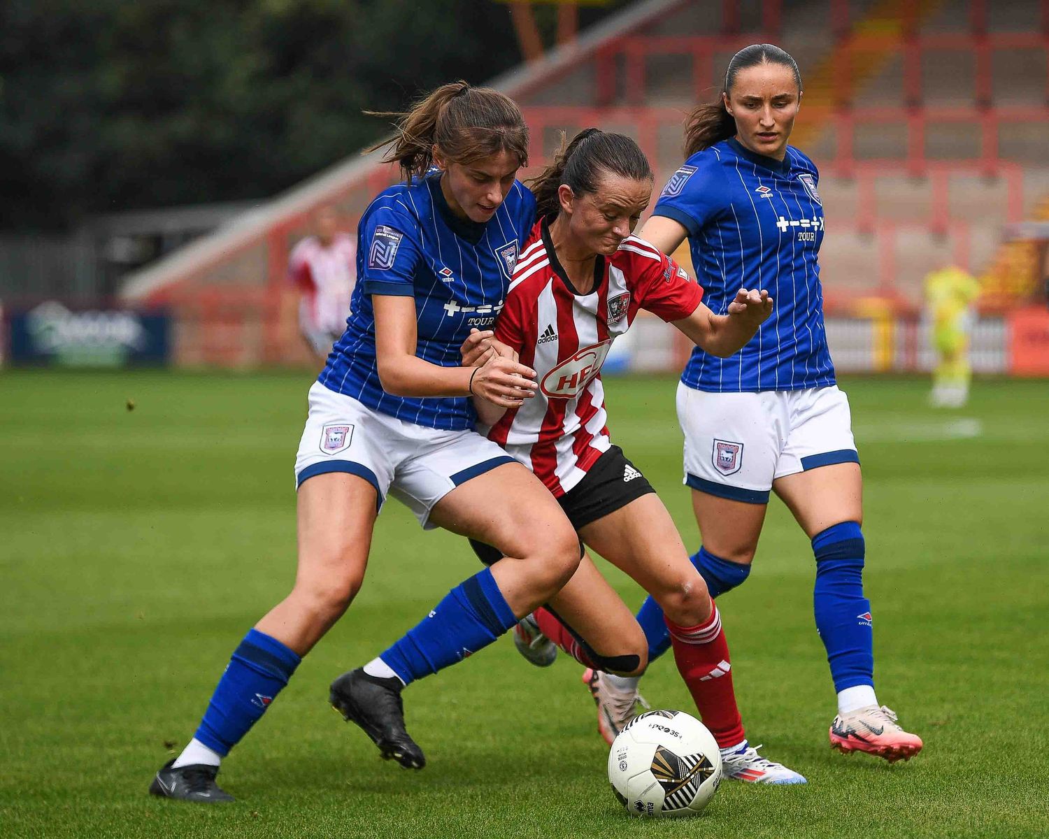 Soccer players compete for the ball in a match between blue and red-striped uniformed teams.