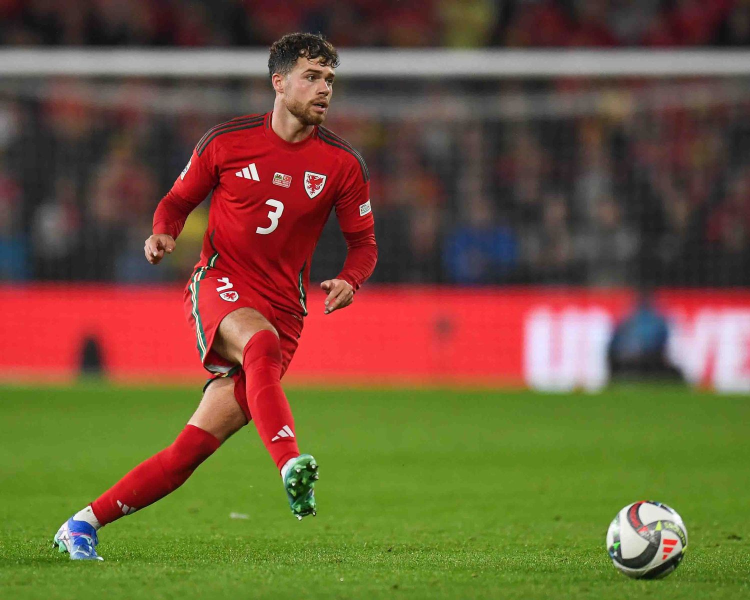 Soccer player in red Wales uniform dribbles the ball during competitive match.
