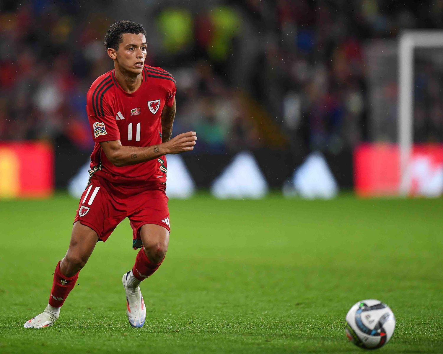 Soccer player in red Wales jersey chases after the ball during competitive match.