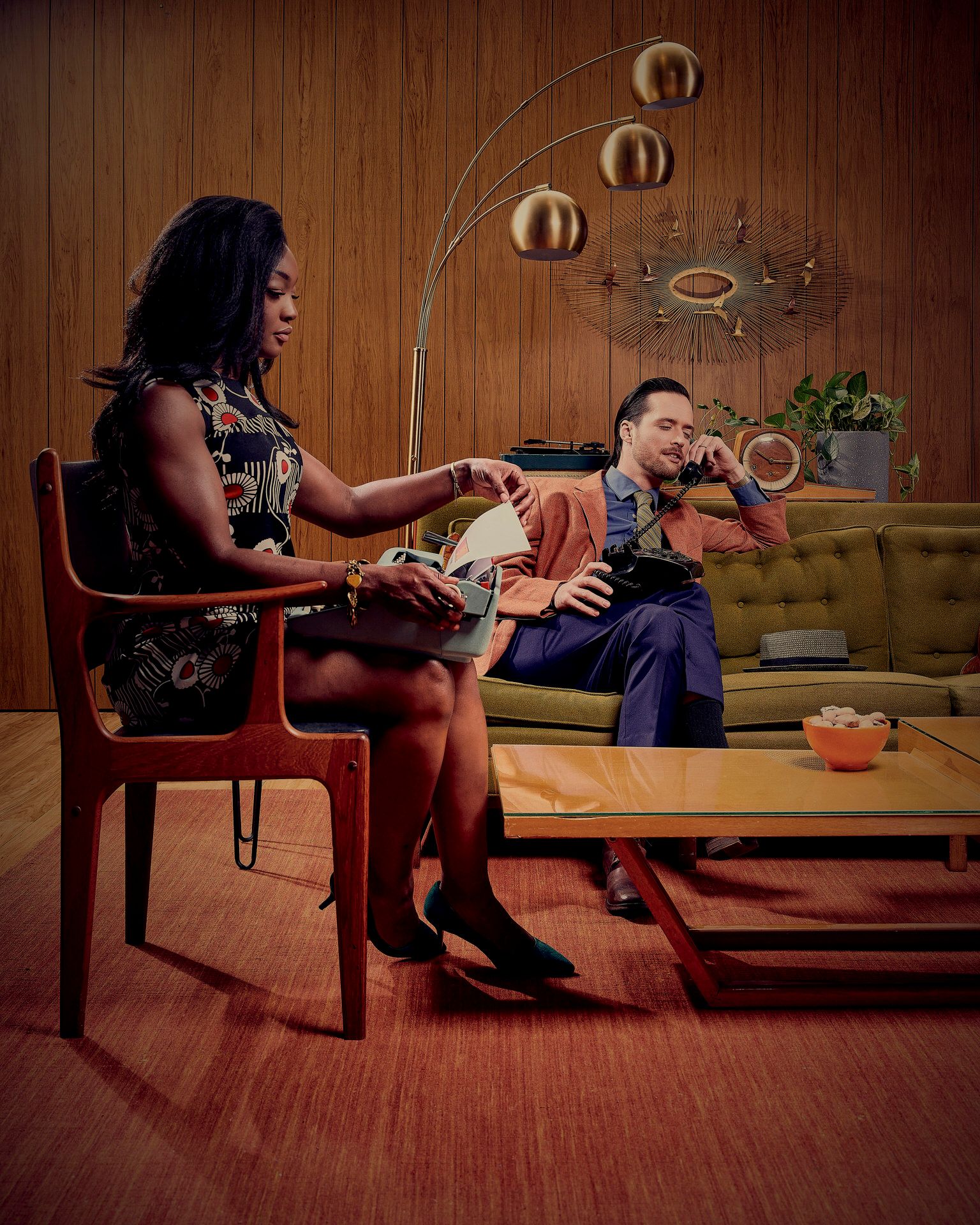 A stylish living room scene with two people on a retro couch and chair set surrounded by vintage decorations.