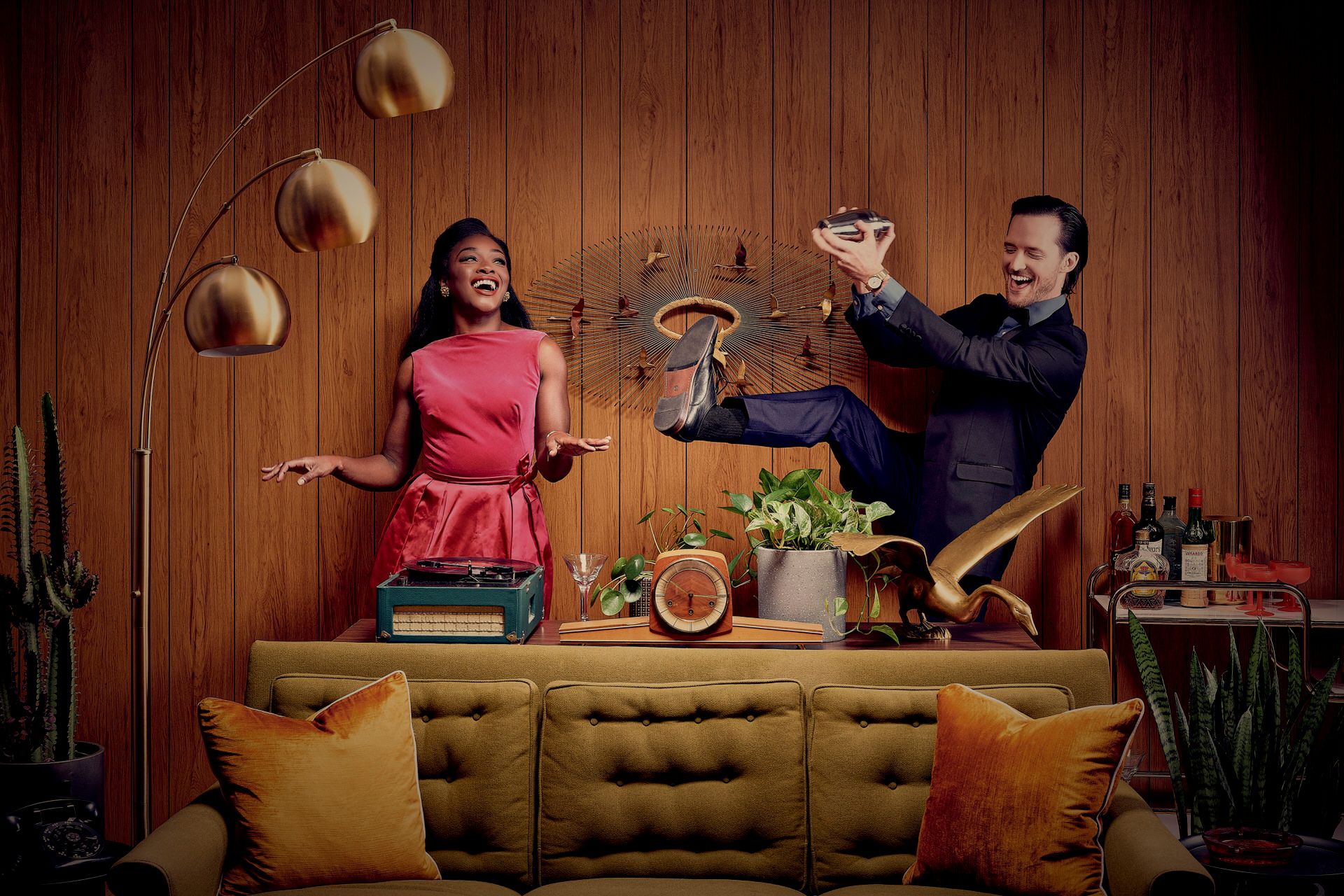 Two people making cocktails behind a yellow couch in a mid-century modern styled room with vintage lighting.
