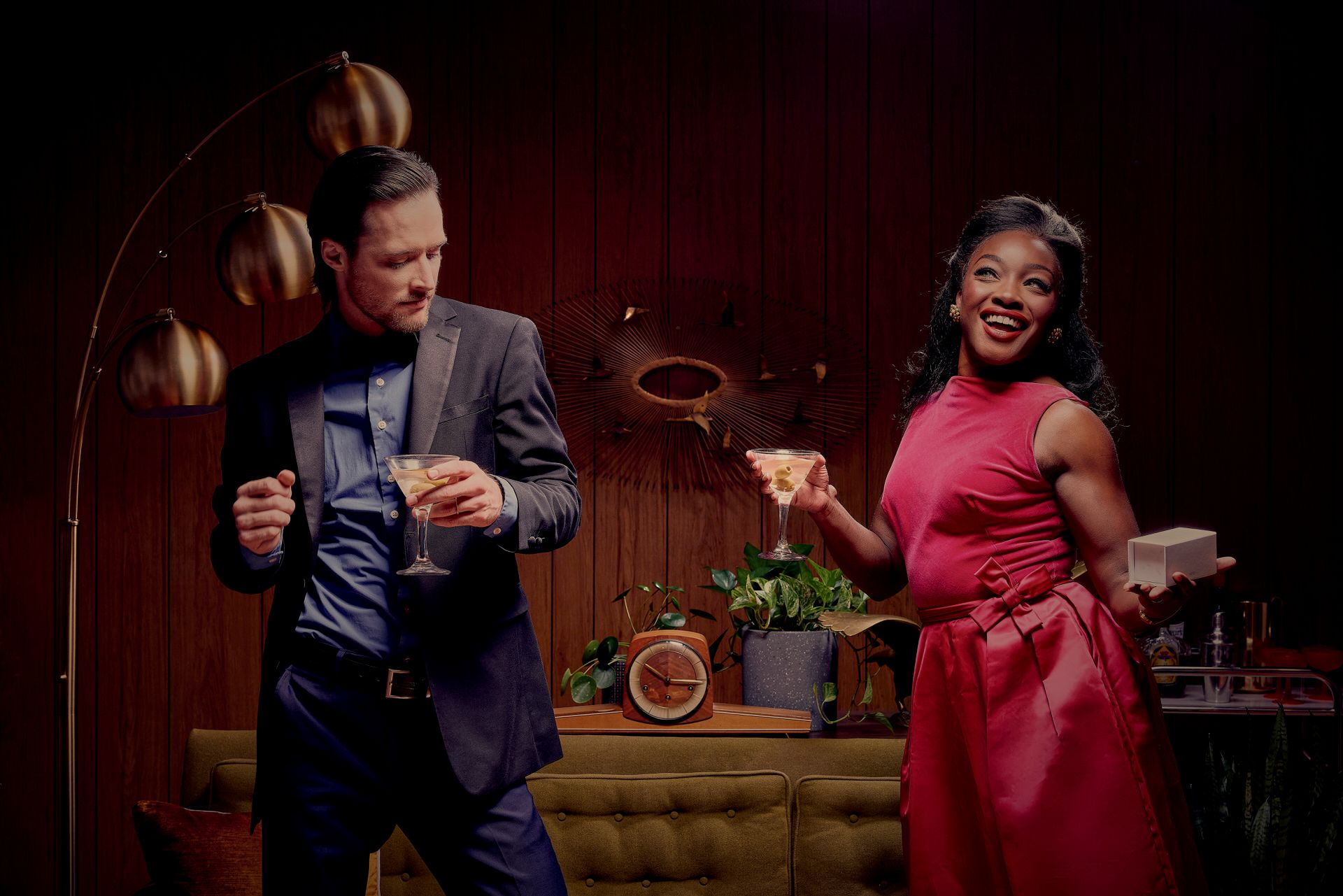 Energetic dance scene with two performers in formal attire against a wood-paneled wall with floating oranges.
