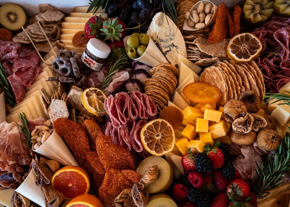 Elaborate charcuterie board with meats, cheeses, crackers, fresh fruits, dried oranges, nuts, and Nutella spread.