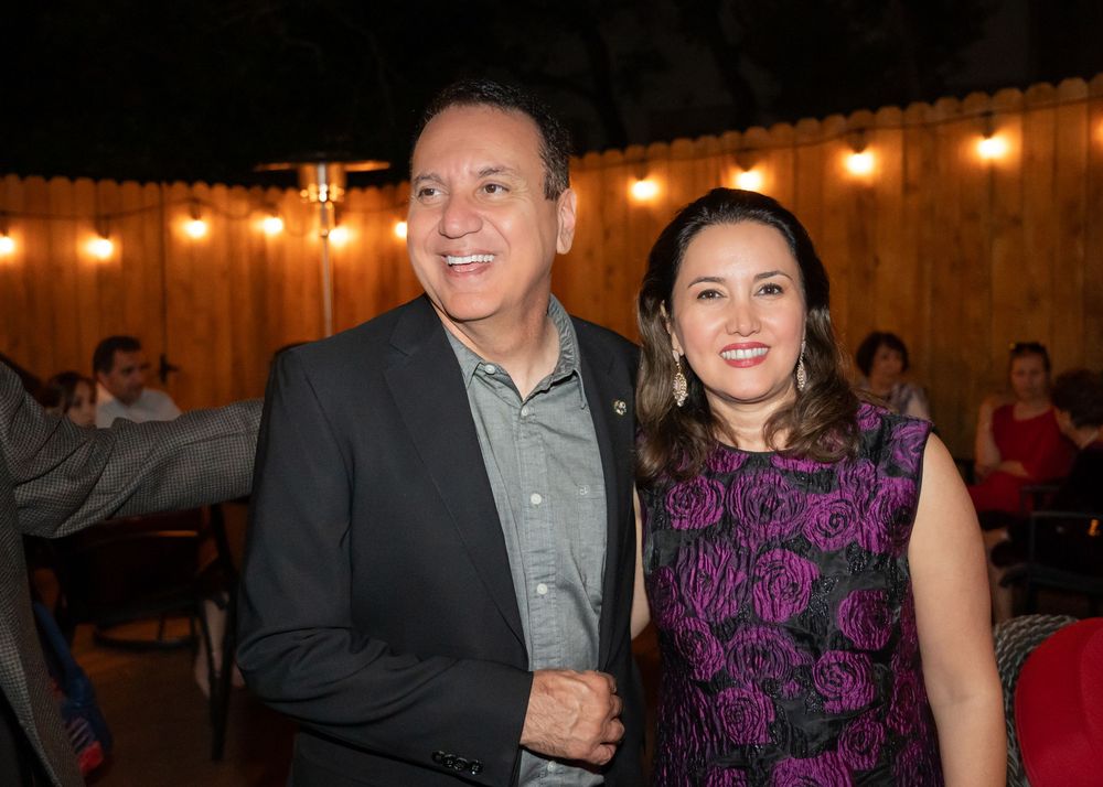 A smiling couple poses together at an outdoor evening party with string lights in the background.