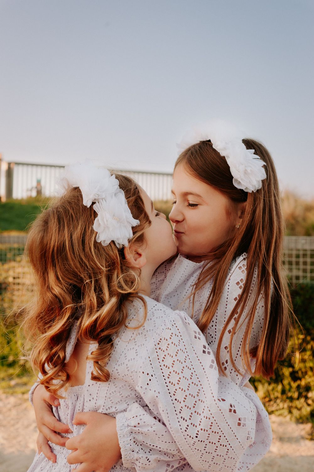 Two children in matching white lace dresses and hair bows share a sweet moment together outdoors.
Altona Family Photographer Melbourne