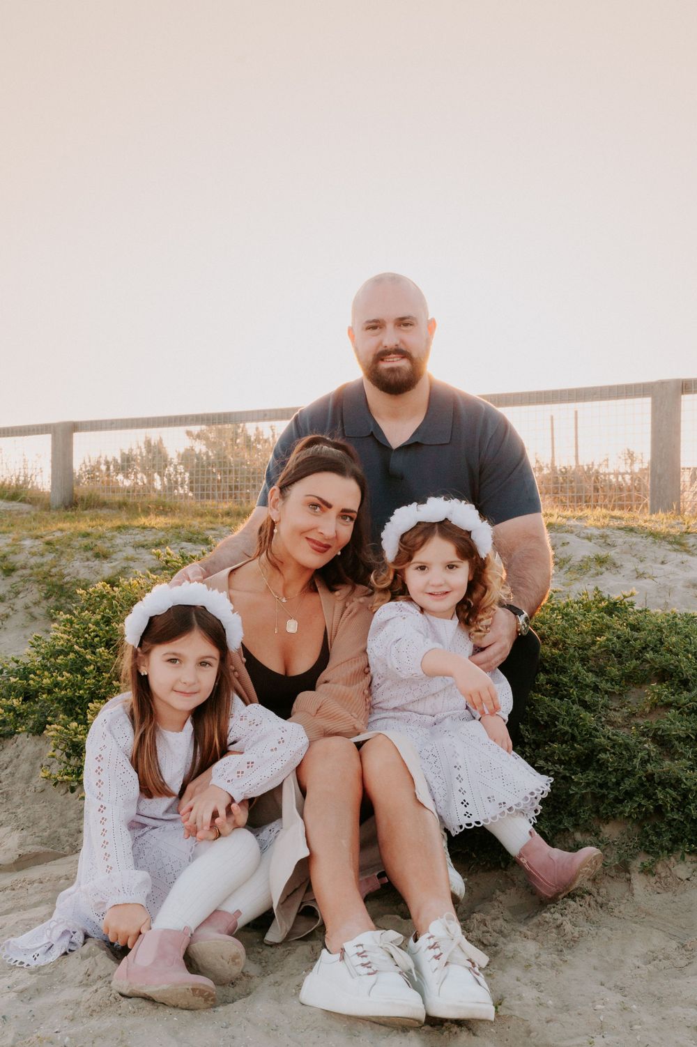 A family sits together on a grassy hillside during sunset wearing coordinated white outfits.
Altona Family Photographer Melbourne