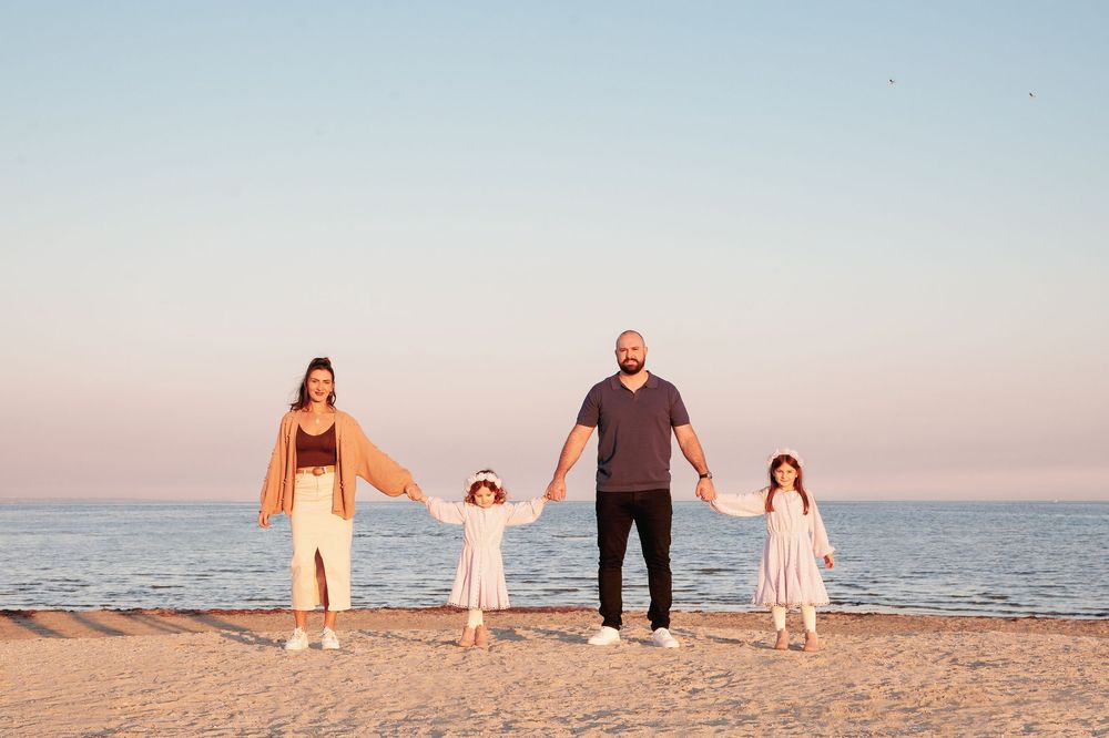A family holds hands while standing together on a sandy beach at sunset with ocean waves behind them.
Altona Family Photographer Melbourne