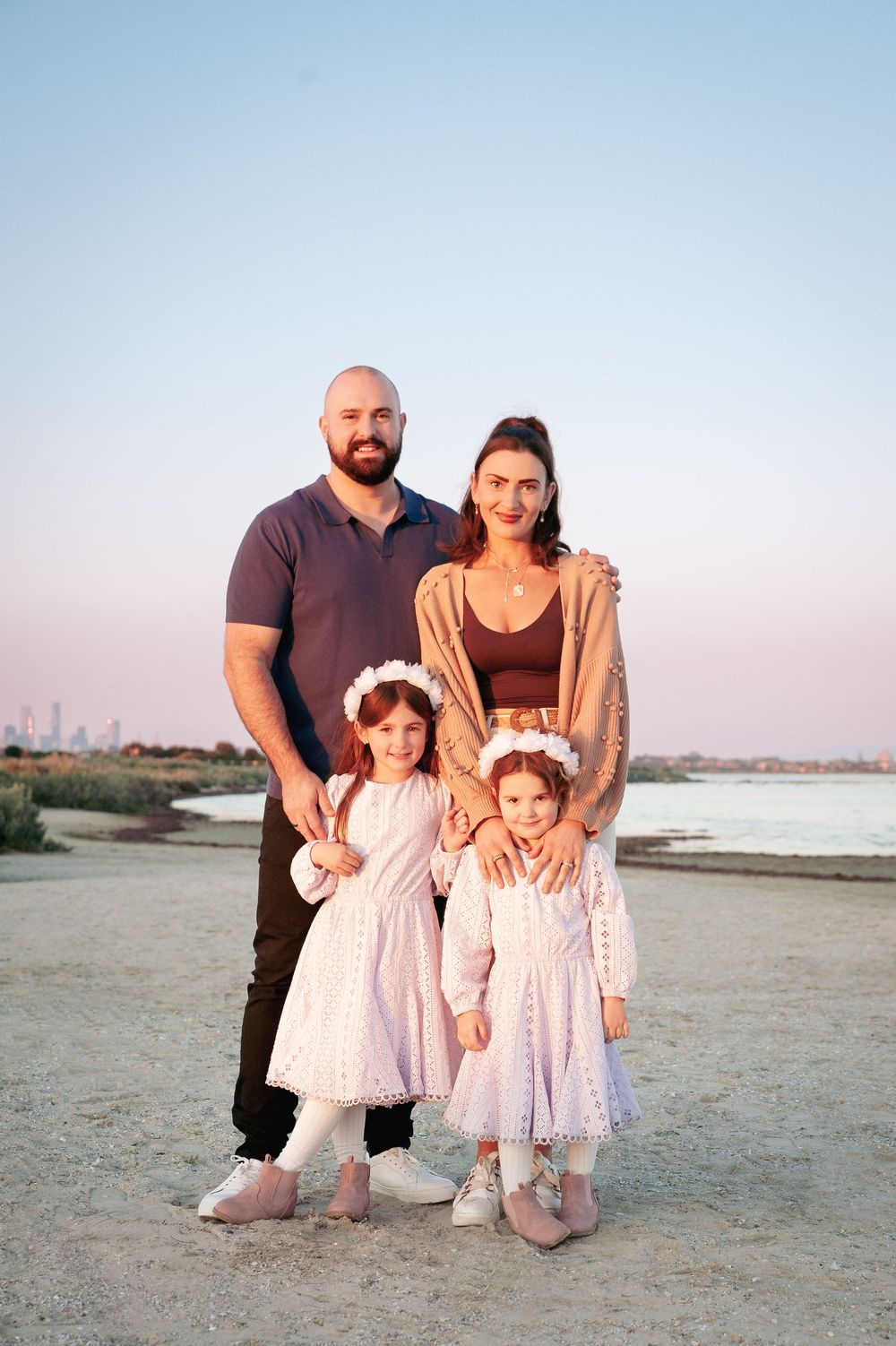 A family of four poses on a beach at sunset, with two young kids wearing white dresses.
Altona Family Photographer Melbourne